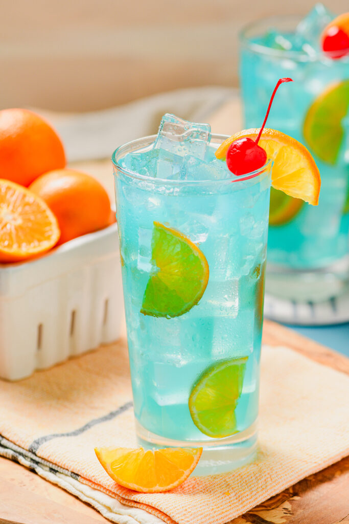 Close up or Blue Lagoon Cocktail with oranges in the background.